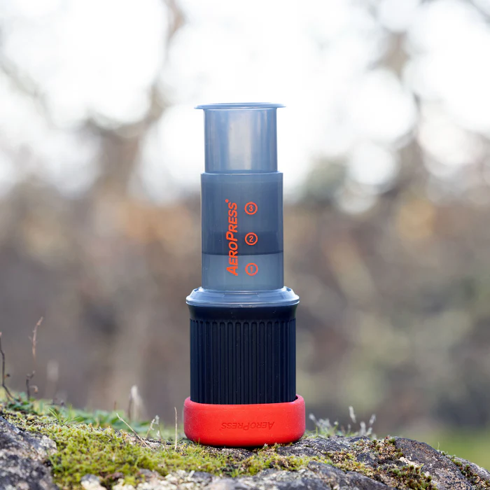 AeroPress Go coffee maker outdoors on a mossy rock – portable brewer ideal for camping, travel, and brewing fresh coffee in nature.